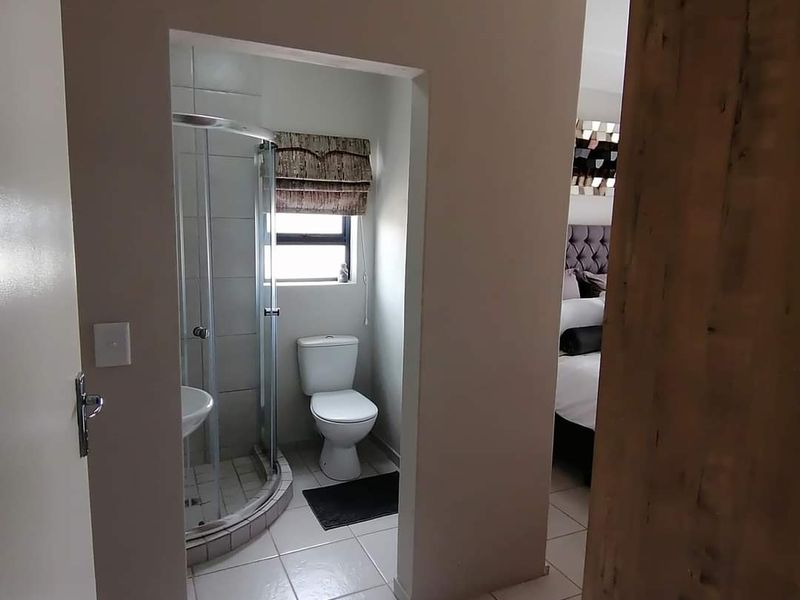 A functional en-suite bathroom featuring a corner shower enclosure, toilet, and tiled flooring, conveniently accessible from the adjacent bedroom.