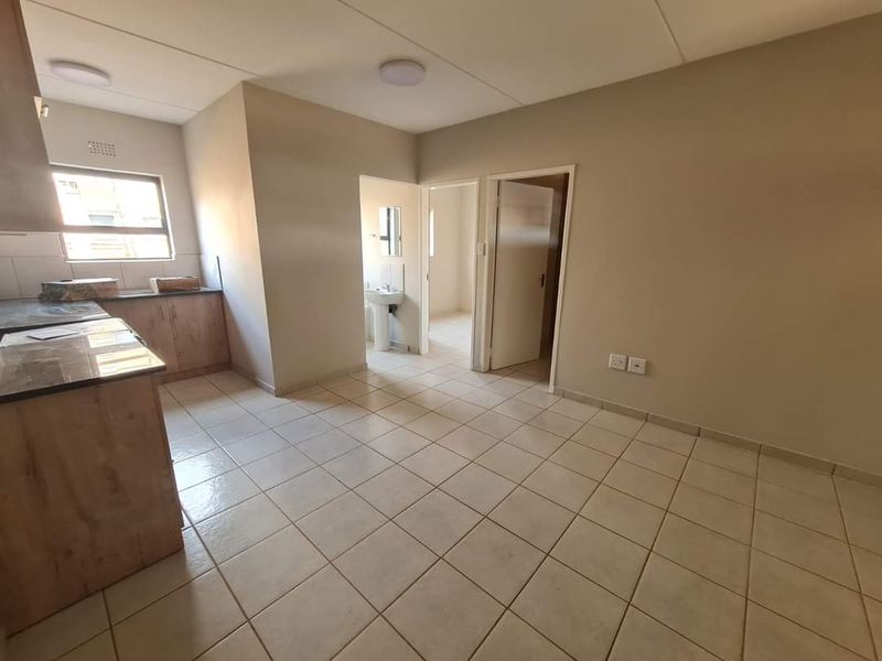 An open-plan kitchen and living area featuring tiled flooring, built-in cabinetry, and direct access to an adjacent bathroom and bedroom.
