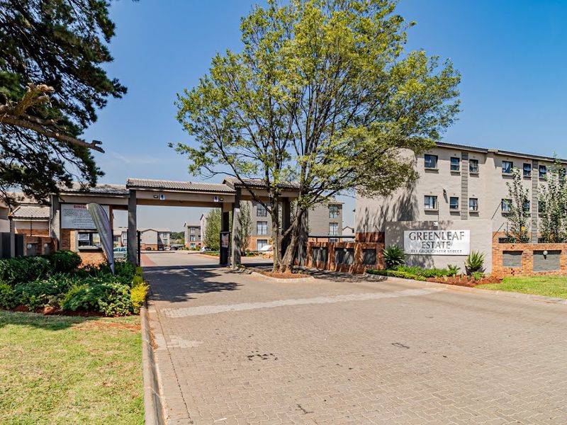 The entrance to Greenleaf Estate featuring a paved driveway, security gate, and brick boundary wall with established landscaping.