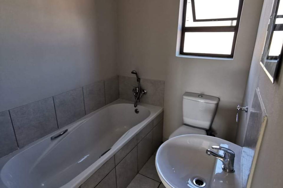A functional bathroom featuring a bathtub, pedestal basin, and toilet with neutral tiled flooring and splashbacks.