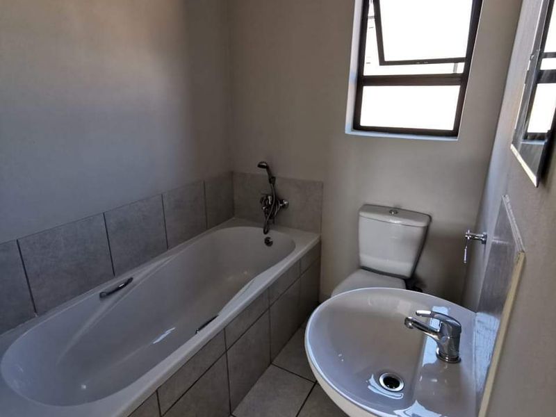 A functional bathroom featuring a bathtub, pedestal basin, and toilet with neutral tiled flooring and splashbacks.