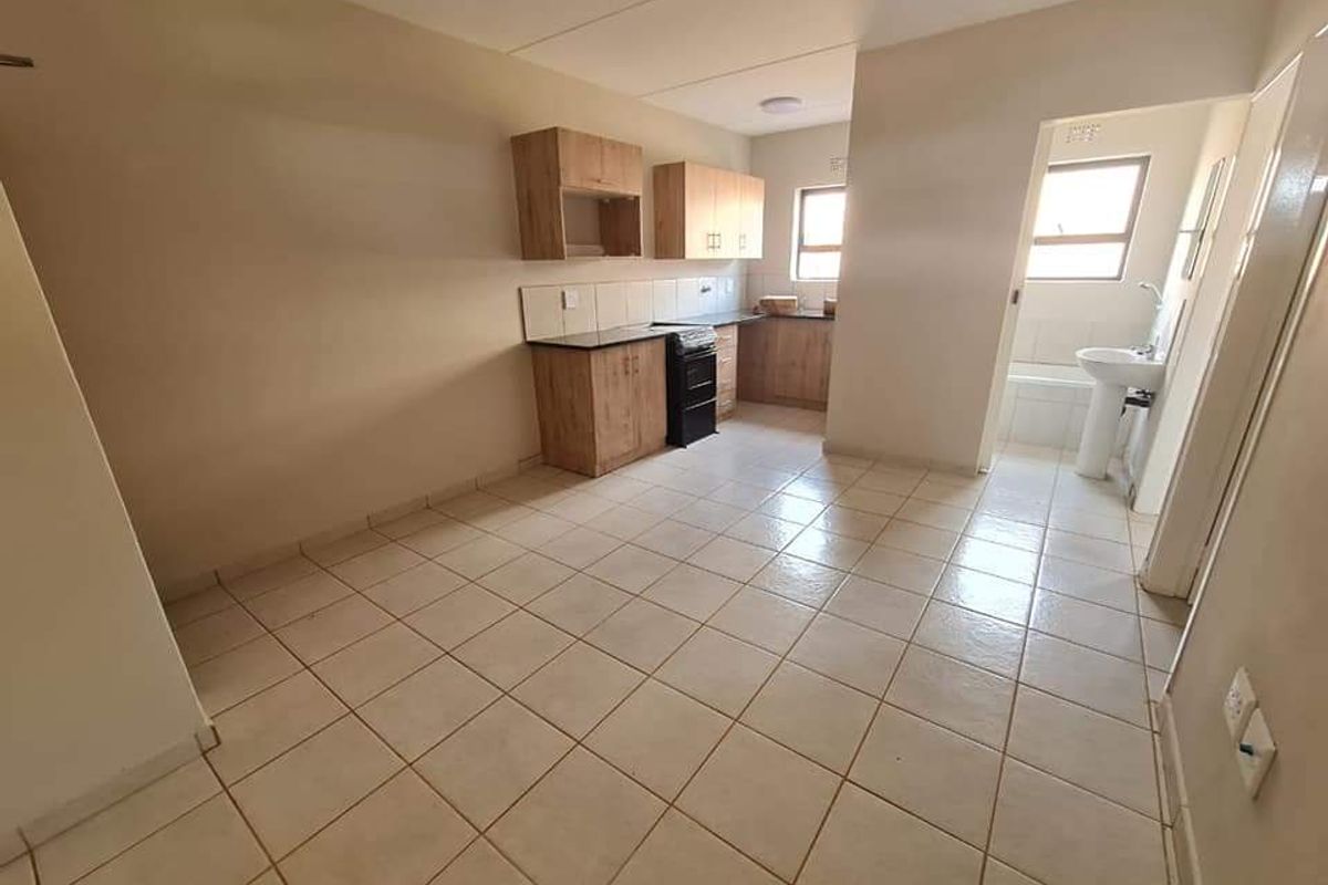 Open-plan kitchen and living area featuring tiled flooring, built-in cabinetry, and an adjacent bathroom with a bathtub and pedestal basin.