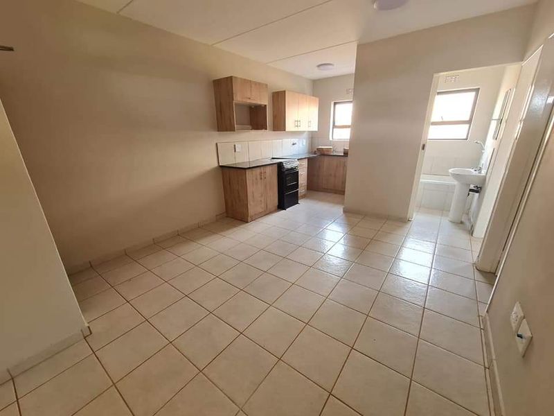 Open-plan kitchen and living area featuring tiled flooring, built-in cabinetry, and an adjacent bathroom with a bathtub and pedestal basin.