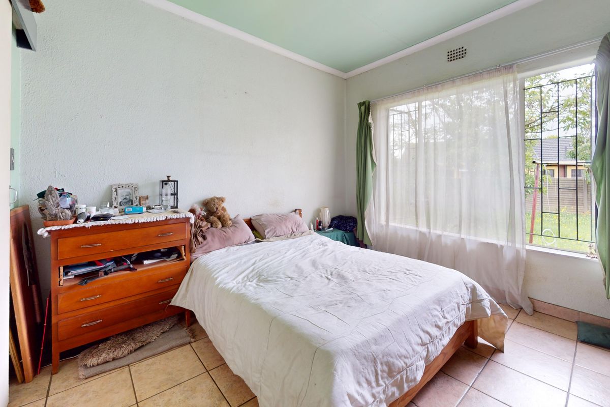 A bedroom featuring tiled flooring, a large window with security bars, and a ceiling vent, requiring cosmetic updates to the walls.
