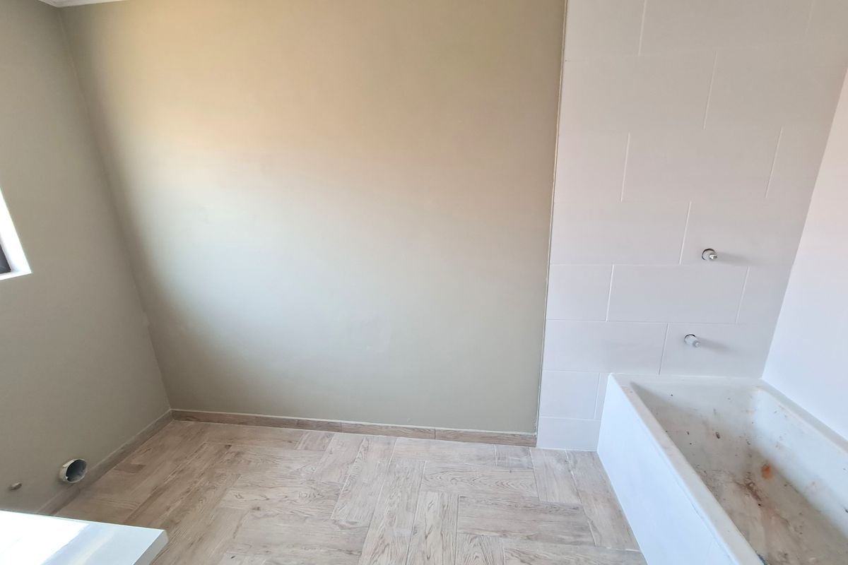 An empty bathroom featuring herringbone floor tiles, a tiled wall section, and a built-in bathtub awaiting final fixture installation.
