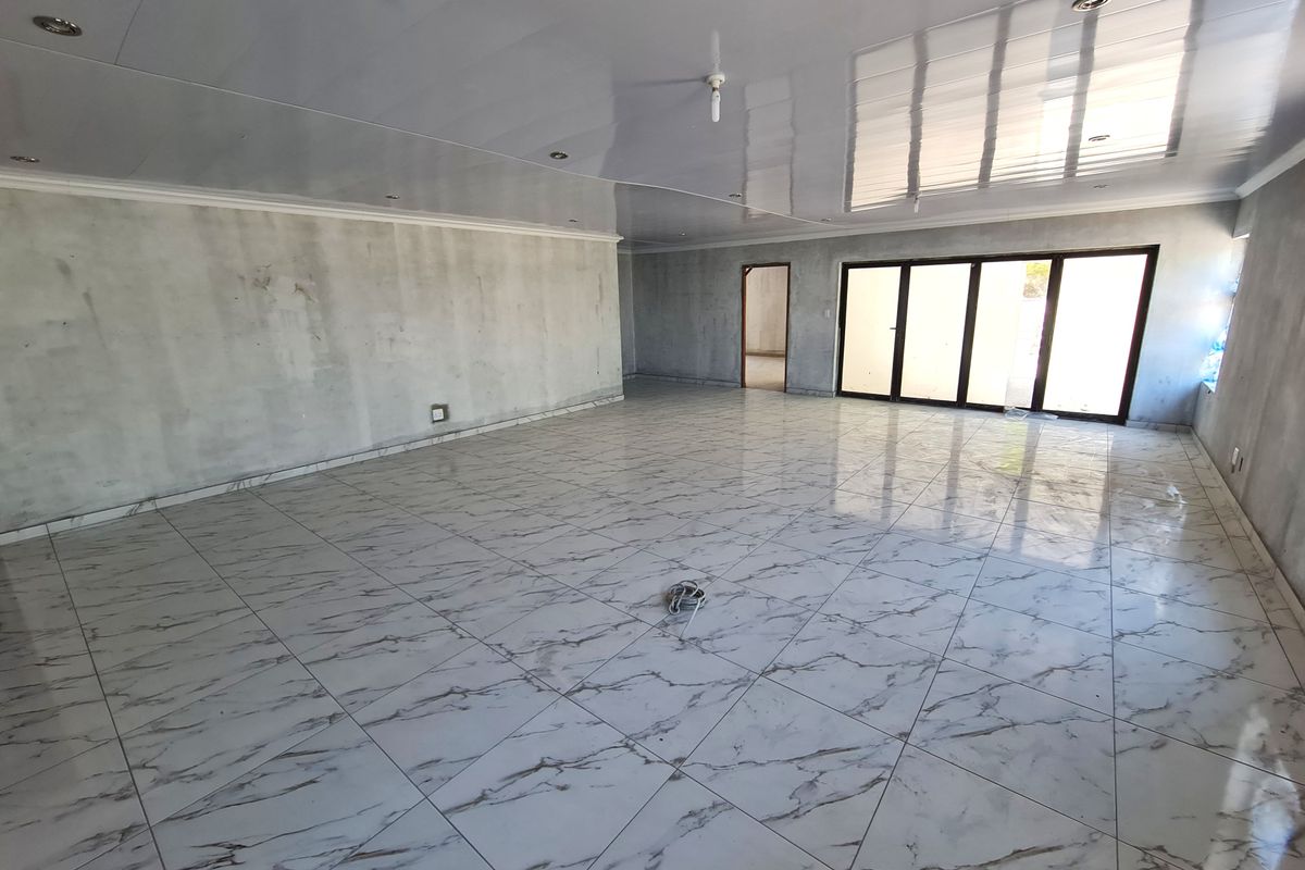 Spacious open-plan living area featuring polished marble-look floor tiles, glossy ceiling panels, and large aluminium sliding doors leading to the exterior.