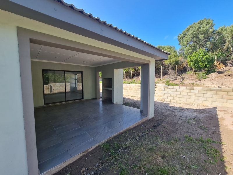 Covered patio area featuring tiled flooring and a built-in braai, providing direct access to the interior through sliding glass doors.