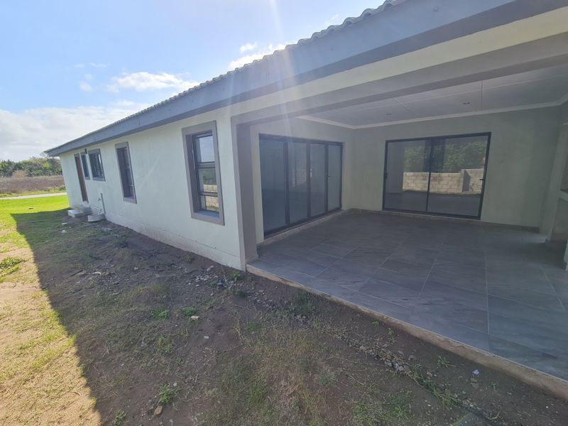 A spacious covered patio featuring modern grey floor tiles, aluminium sliding and folding doors, and recessed ceiling lighting, overlooking an unfinished garden area.
