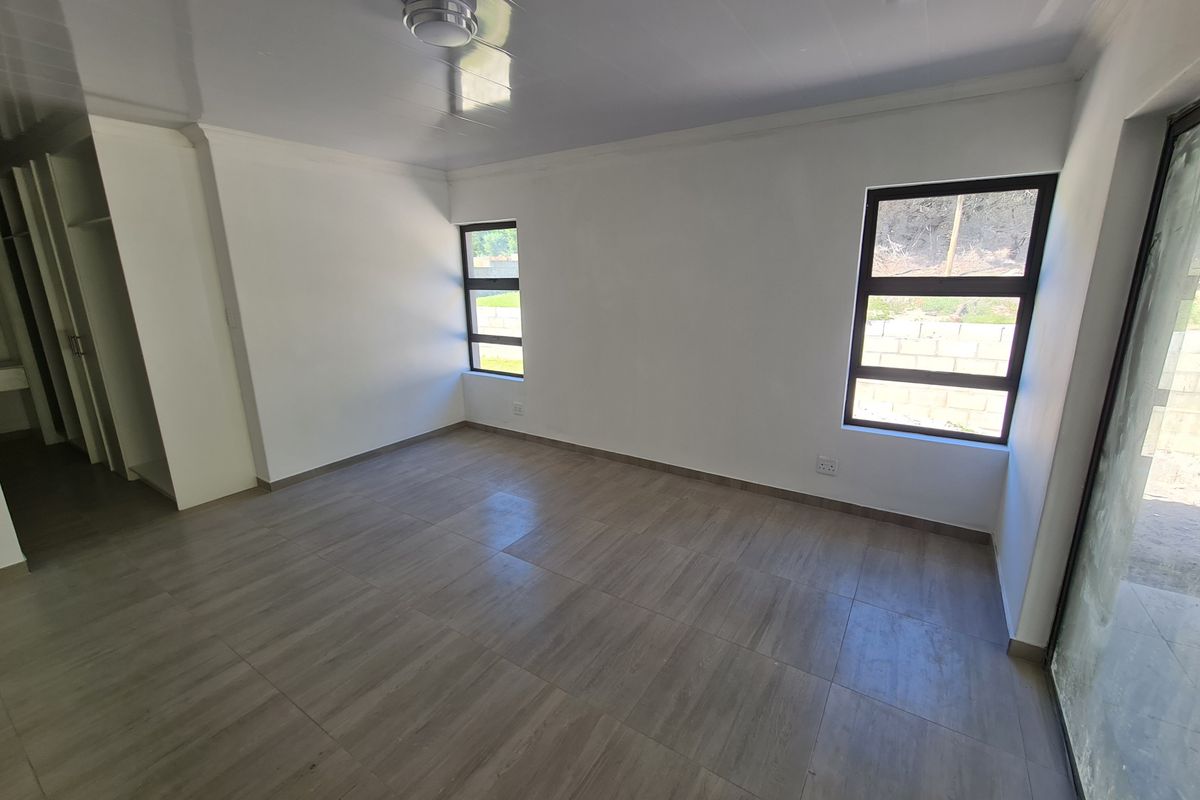 A bright, empty bedroom featuring modern tiled flooring, built-in cupboards, and large aluminium-framed windows providing natural light.