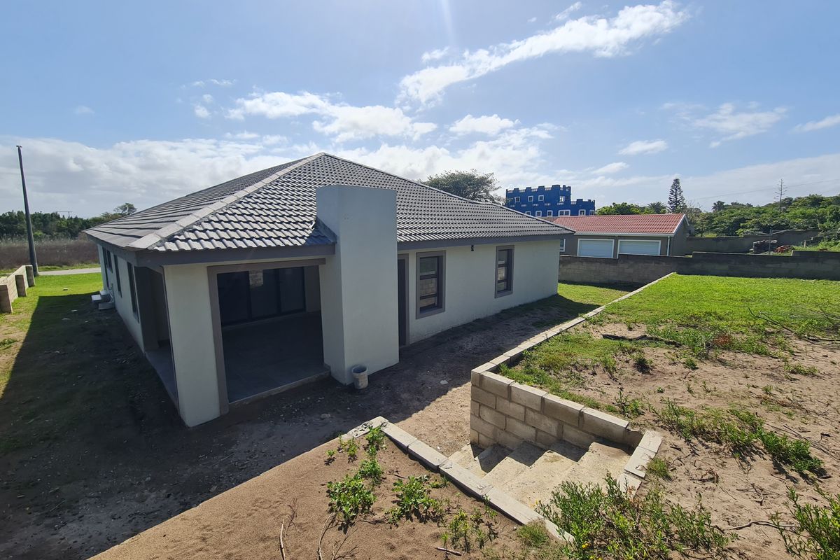 Rear view of the property featuring a covered patio, tiled roof, and unfinished garden area with concrete retaining walls and stairs.