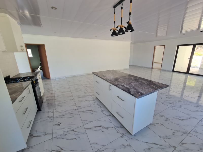 Spacious open-plan kitchen and living area featuring modern white cabinetry, stone countertops, a central island, and polished marble-look tiled flooring.
