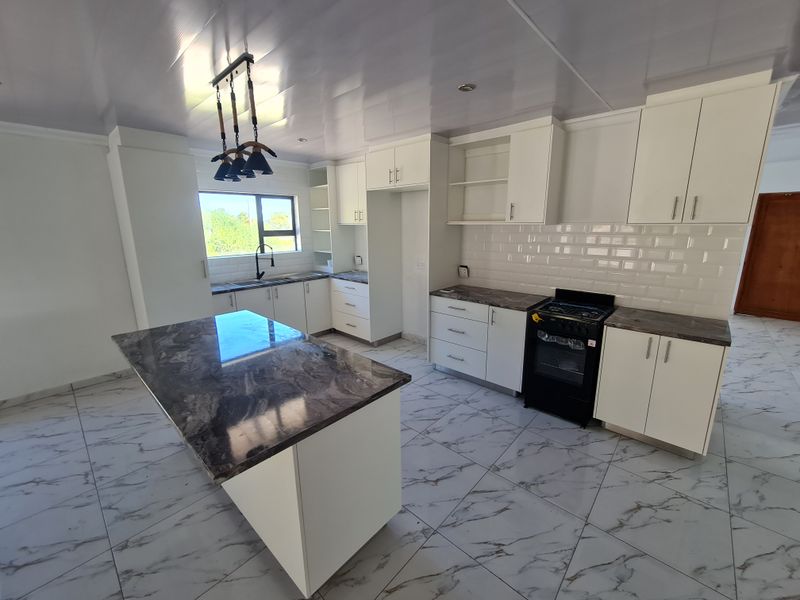 Modern kitchen featuring a central island, marble-look countertops, white cabinetry, subway tile backsplash, and tiled flooring in a bright, open-plan layout.