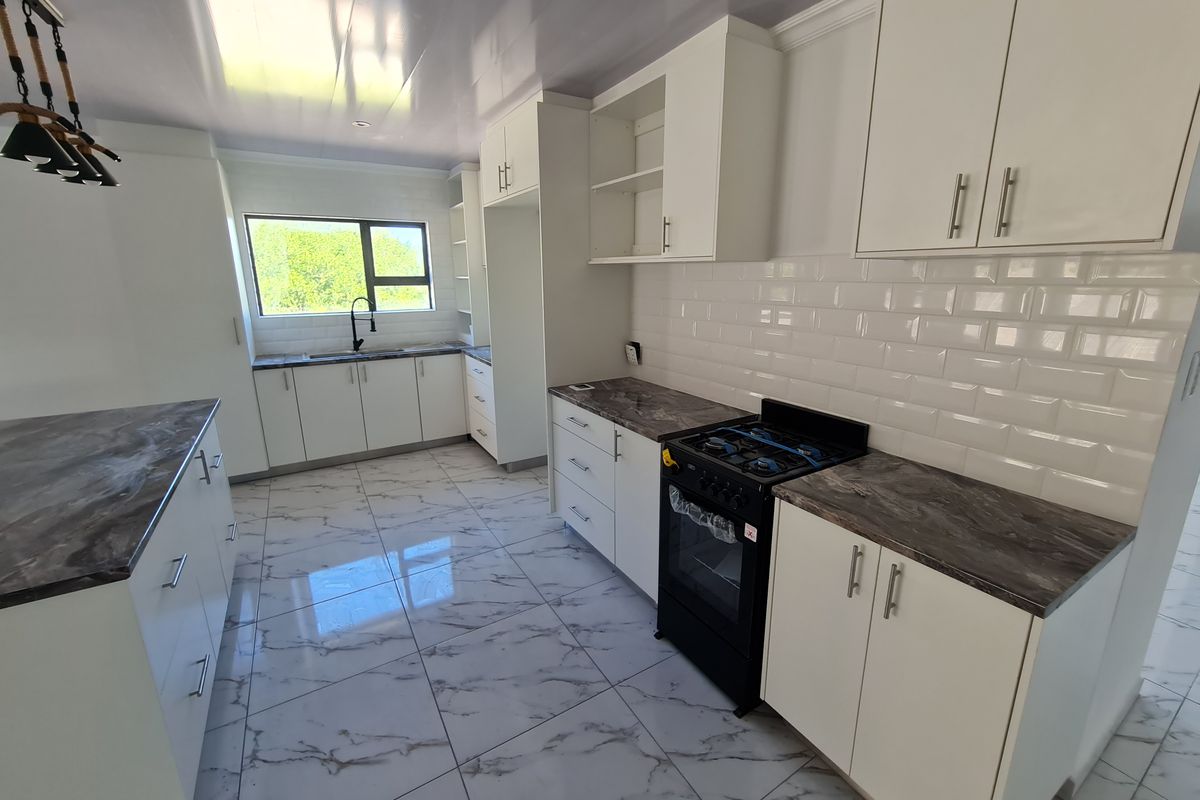 Modern, bright kitchen featuring white cabinetry, marble-effect countertops, subway tile backsplash, and a freestanding gas stove with high-quality floor tiling.