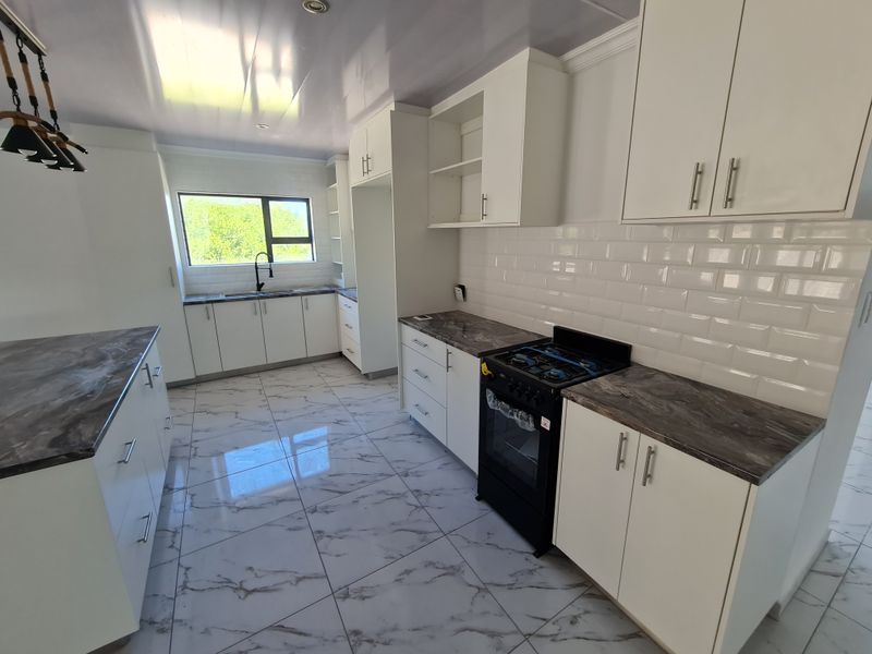 Modern, bright kitchen featuring white cabinetry, marble-effect countertops, subway tile backsplash, and a freestanding gas stove with high-quality floor tiling.