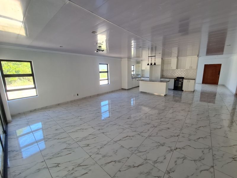 Spacious open-plan living area featuring polished marble-look floor tiles, a modern kitchen with island, and ample natural light from large windows.