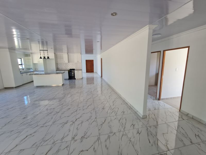 Spacious open-plan living area featuring a modern kitchen with a central island, sleek cabinetry, and polished marble-look tiled flooring throughout.
