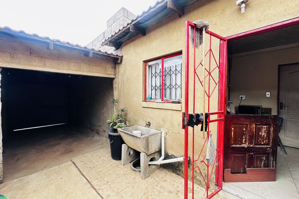 Rear exterior area featuring a concrete laundry basin, tiled patio, and access to a covered garage space with security gate.
