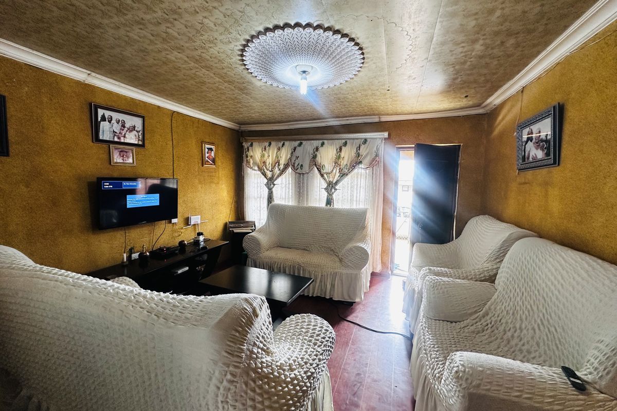 A living room featuring textured walls, a decorative ceiling rose, and laminate flooring, offering a dated aesthetic with potential for modernization.
