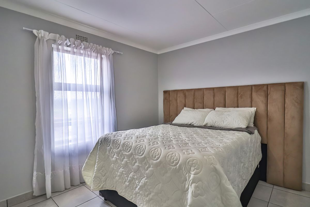 A well-maintained bedroom featuring neutral grey walls, tiled flooring, and a large window with sheer curtains.