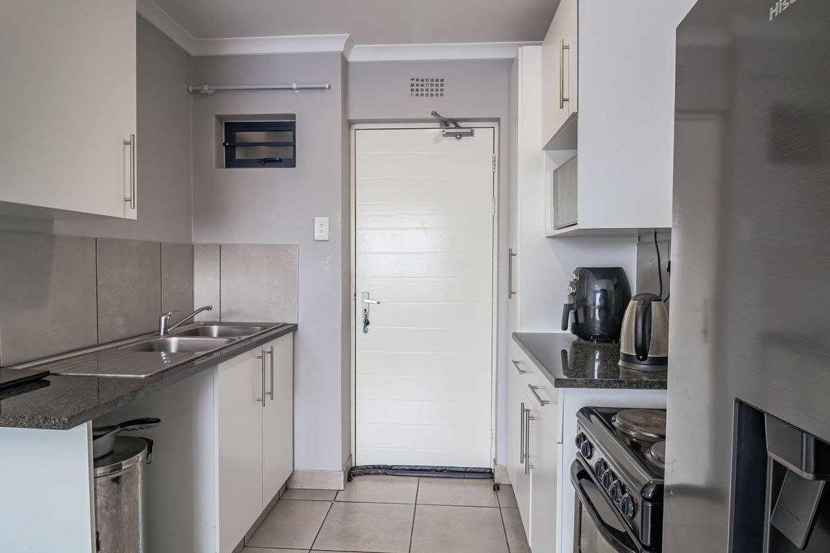 A functional kitchen featuring white cabinetry, granite countertops, a stainless steel double sink, and tiled flooring with direct access to an exterior door.