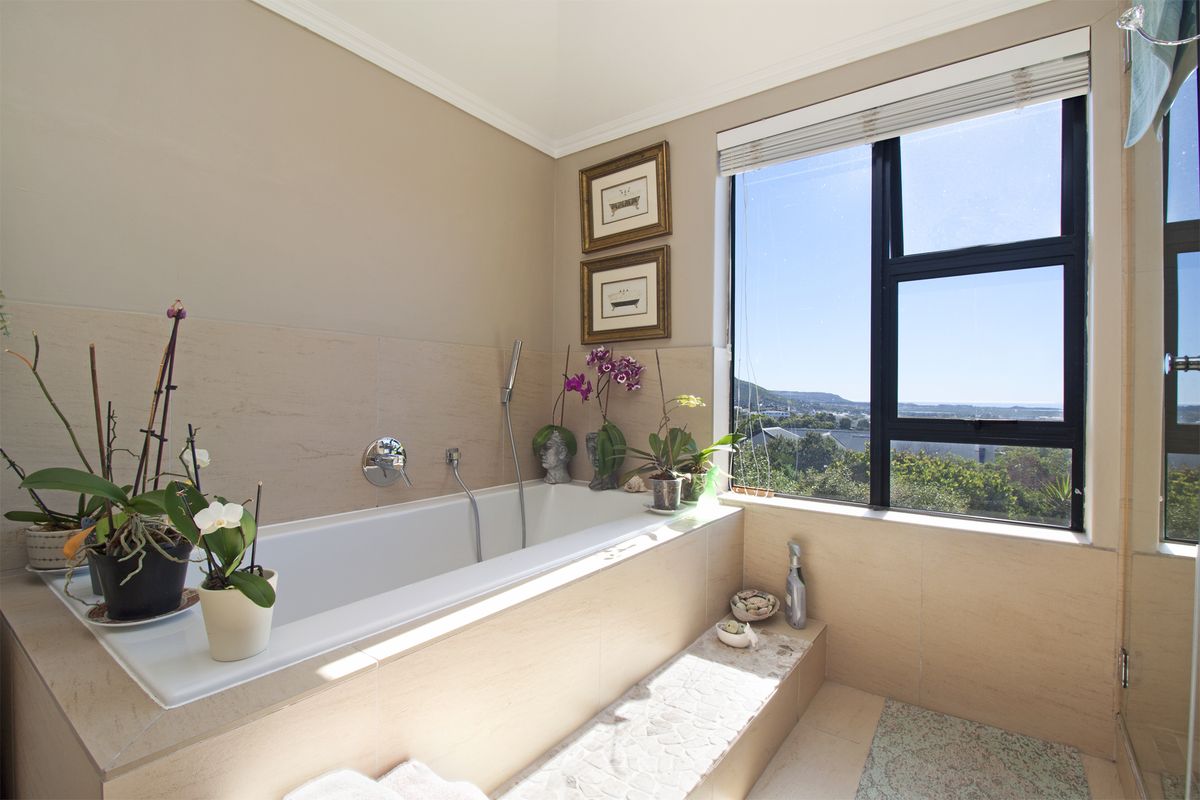 A bright bathroom featuring a built-in bathtub with tiled surround, large window with scenic views, and modern chrome fixtures.
