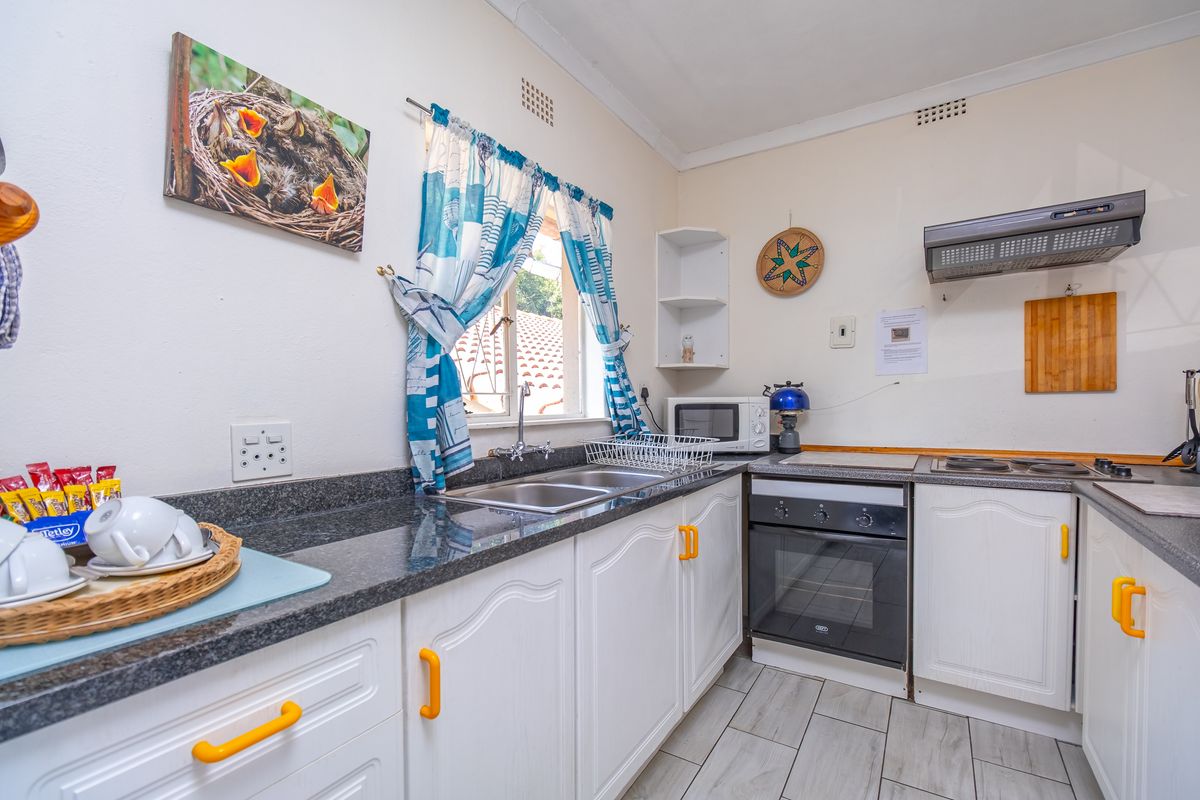 A functional kitchen featuring white cabinetry, granite countertops, a double basin sink, and built-in cooking appliances including an oven and hob.