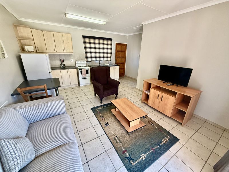 Open-plan living area featuring a functional kitchen with built-in cabinetry, a freestanding stove, and tiled flooring throughout the combined space.