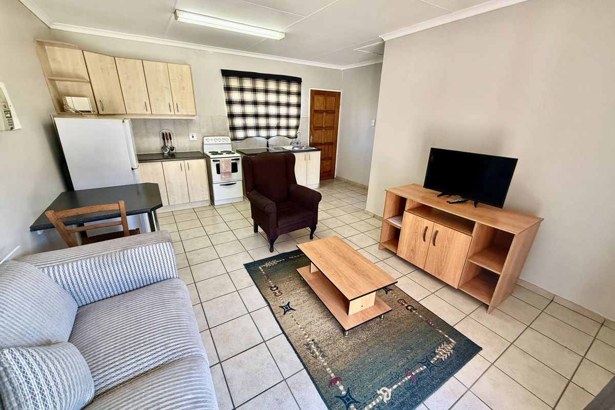 Open-plan living area featuring a functional kitchen with built-in cabinetry, a freestanding stove, and tiled flooring throughout the combined space.
