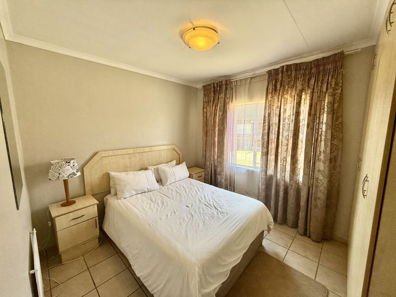 A functional bedroom featuring tiled flooring, a built-in wardrobe, and a central ceiling light fixture, offering a neutral and practical living space.