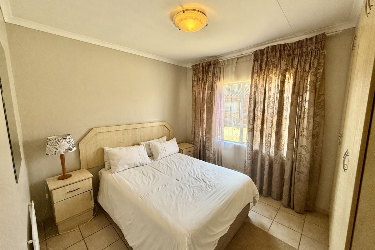 A functional bedroom featuring tiled flooring, a built-in wardrobe, and a central ceiling light fixture, offering a neutral and practical living space.