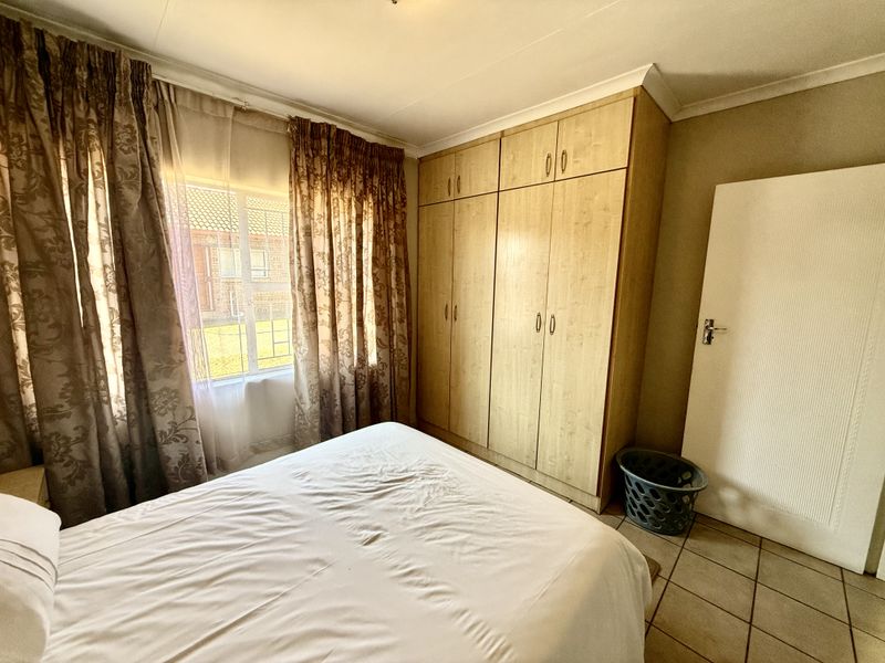 A bedroom featuring built-in wooden cupboards, tiled flooring, and a window with curtains, providing a functional and well-lit living space.