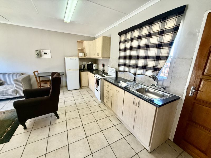 Open-plan kitchen and living area featuring light wood cabinetry, laminate countertops, stainless steel sink, and tiled flooring throughout.
