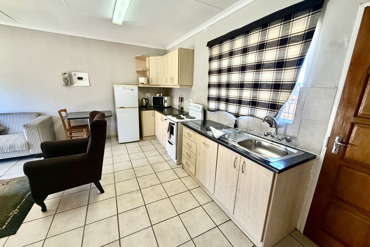 Open-plan kitchen and living area featuring light wood cabinetry, laminate countertops, stainless steel sink, and tiled flooring throughout.