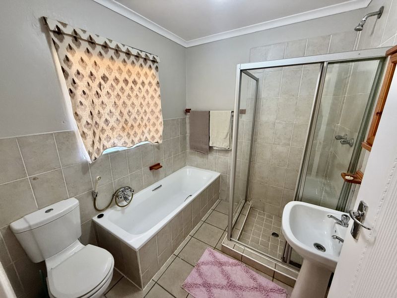 A functional bathroom featuring a built-in bathtub, separate shower enclosure, pedestal basin, and toilet with neutral wall and floor tiling.