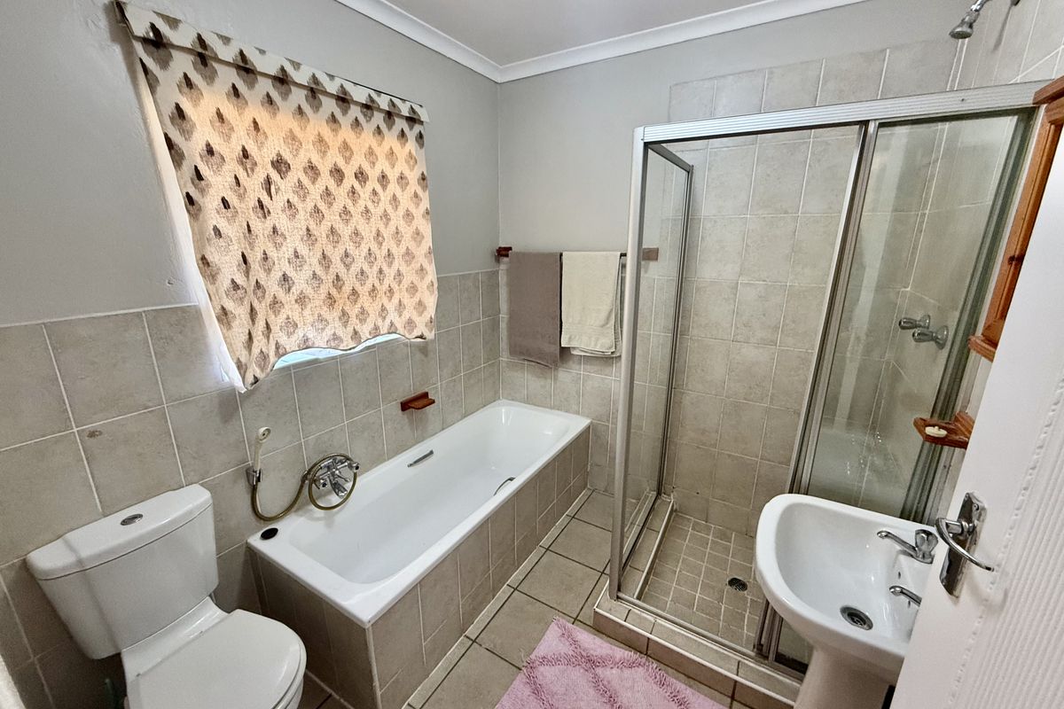 A functional bathroom featuring a built-in bathtub, separate shower enclosure, pedestal basin, and toilet with neutral wall and floor tiling.