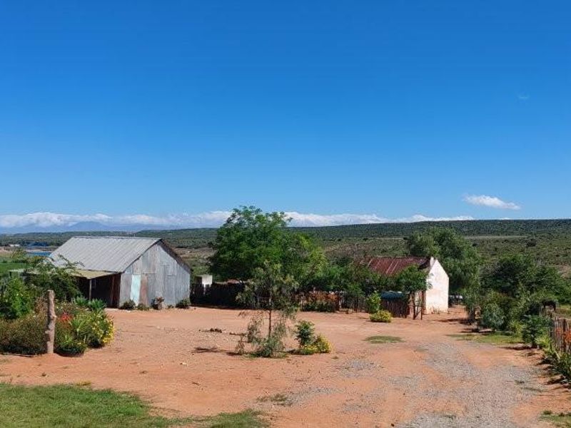 A wide-angle view of a rural farm property featuring rustic outbuildings, open land, and a natural landscape setting.