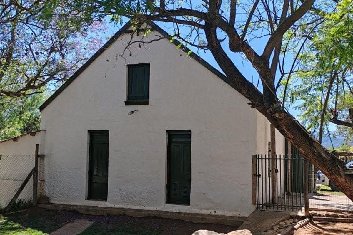 A view of the rear exterior of the farm building, featuring a white textured facade, dark green doors, and surrounding garden area.
