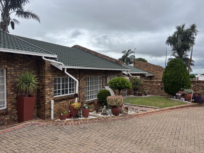 A well-maintained face brick house exterior featuring a tiled roof, paved driveway, and established garden beds along the front facade.
