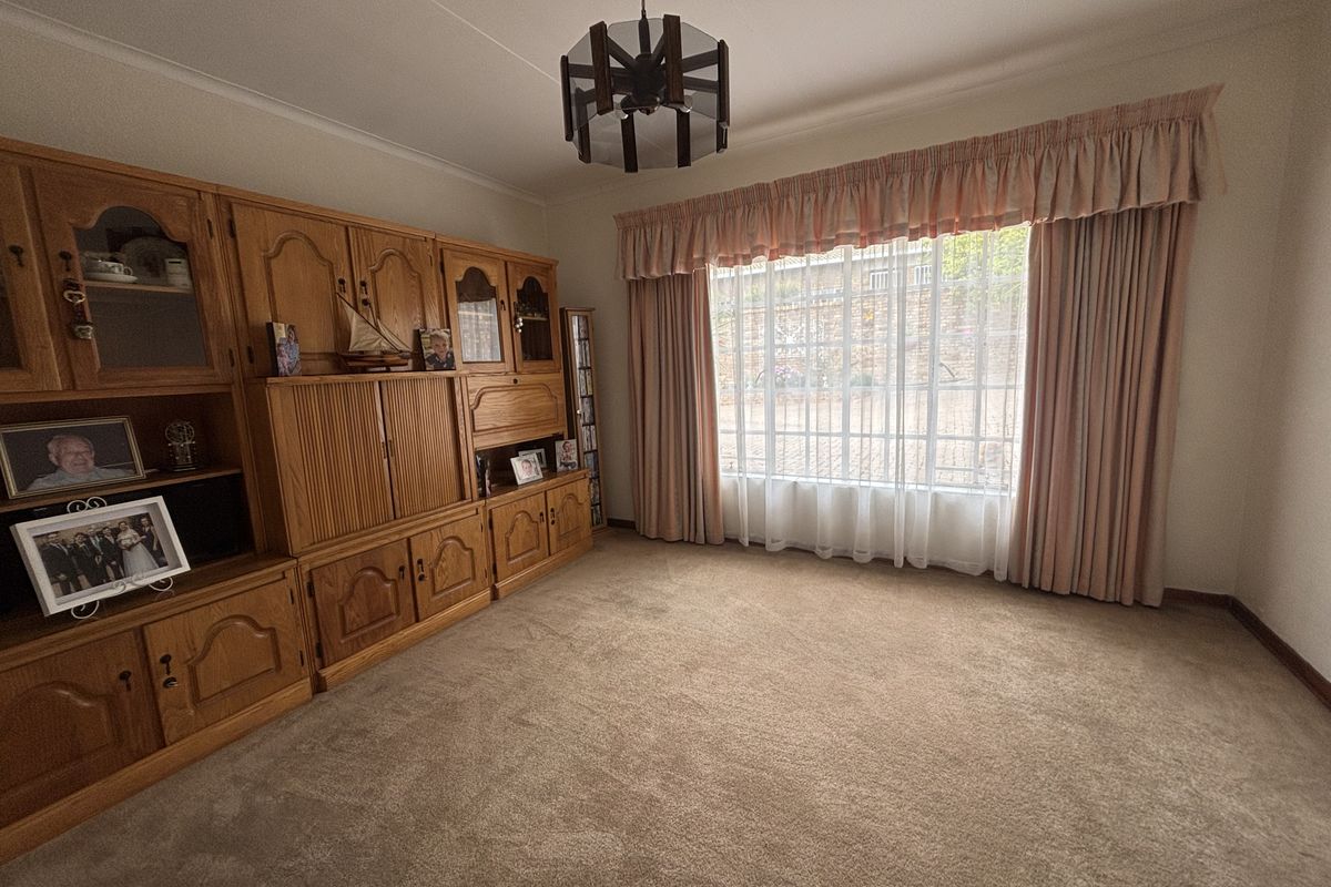 A living room featuring wall-to-wall carpeting, a large window with curtains, and built-in wooden cabinetry.