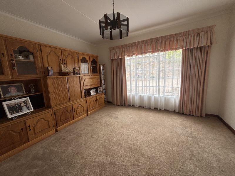 A living room featuring wall-to-wall carpeting, a large window with curtains, and built-in wooden cabinetry.
