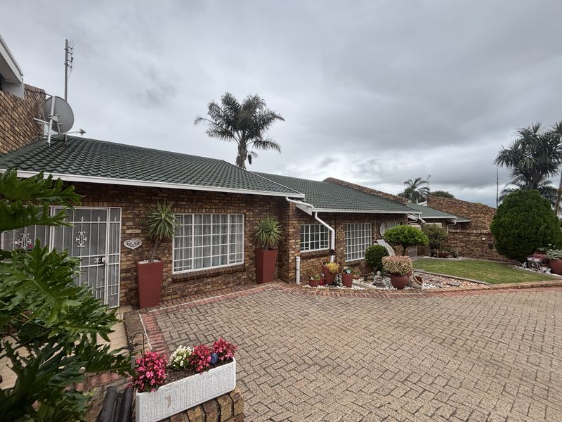 Front elevation of a brick house featuring a tiled roof, paved driveway, and secure entrance gate.