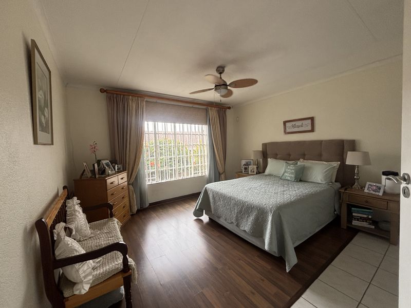 A well-maintained bedroom featuring laminate flooring, a ceiling fan, and security bars on the window.