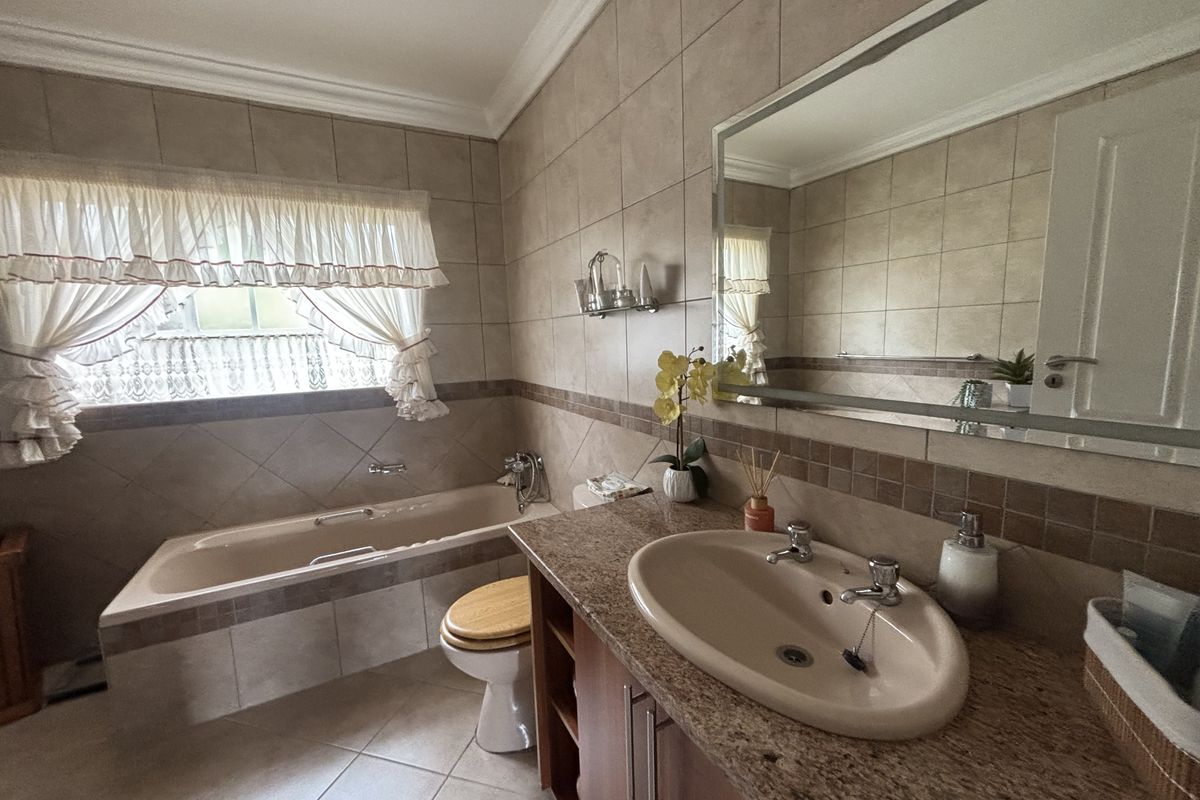 A functional bathroom featuring a built-in bathtub, granite-topped vanity with a ceramic basin, and neutral wall and floor tiling.