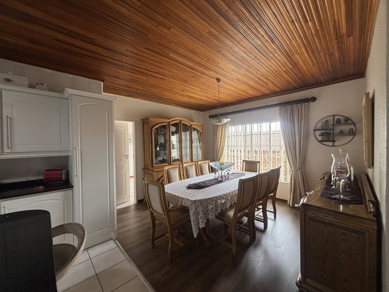 Open plan dining area featuring a warm timber tongue and groove ceiling, laminate flooring, and an adjacent kitchen with white cabinetry.