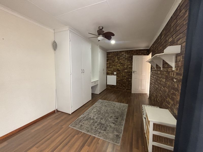 Bedroom featuring laminate flooring, an exposed brick feature wall, built-in cupboards, and a ceiling fan.