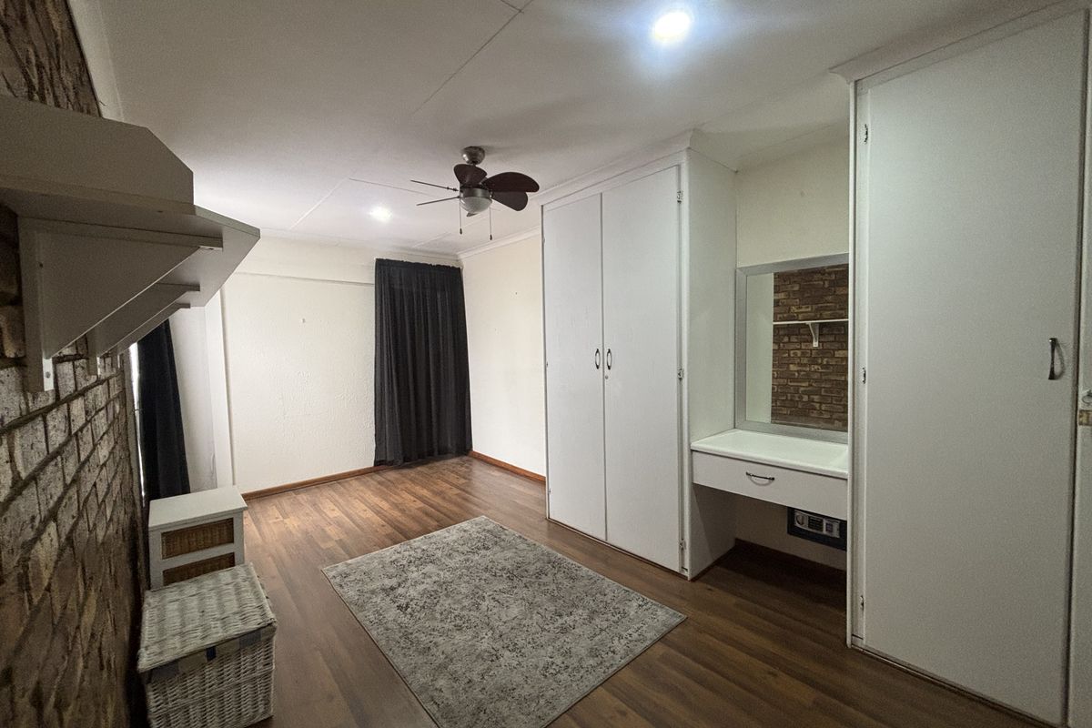 Bedroom featuring laminate flooring, exposed brick accent wall, built-in cupboards with integrated vanity, and a ceiling fan.