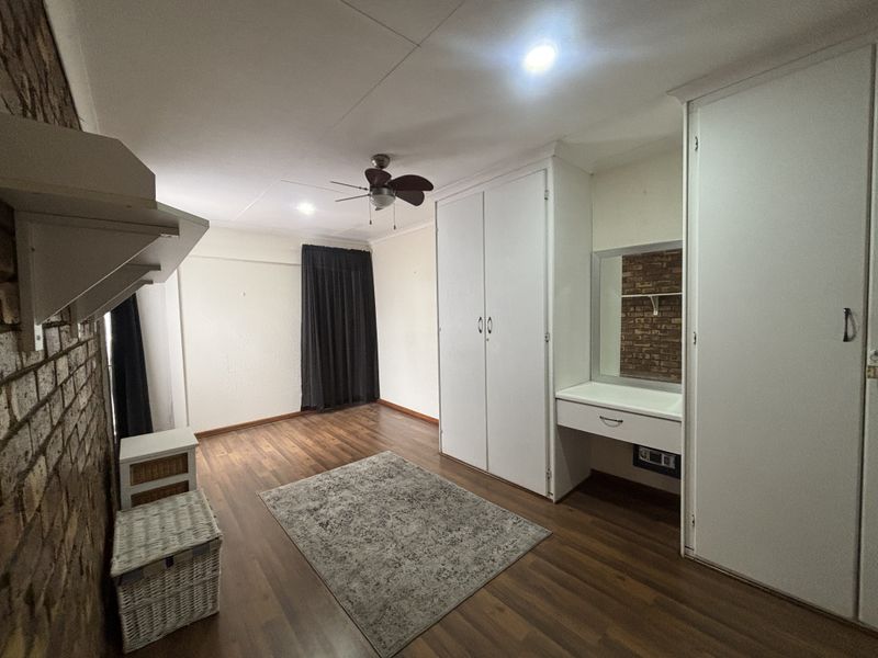 Bedroom featuring laminate flooring, exposed brick accent wall, built-in cupboards with integrated vanity, and a ceiling fan.