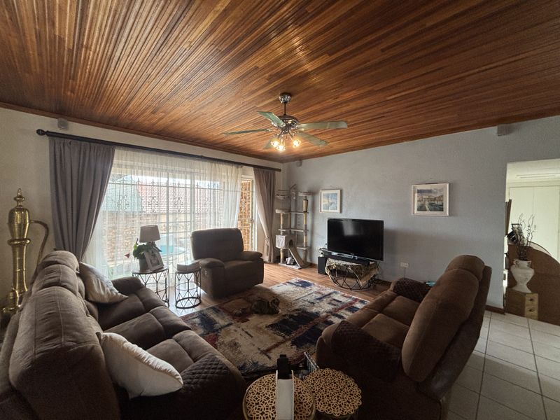 A comfortable living room featuring a warm timber tongue and groove ceiling, ceiling fan, and large sliding glass doors leading to the outdoor area.