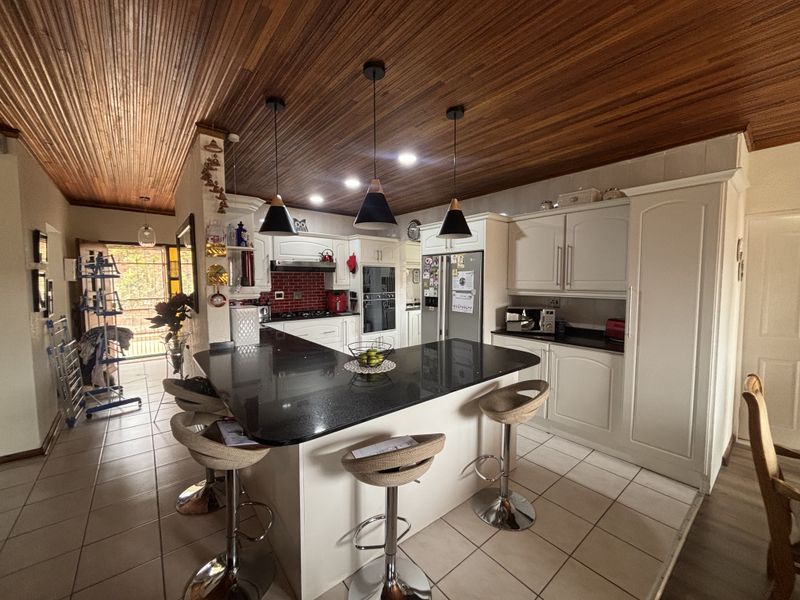 Spacious kitchen featuring a central island with granite countertops, built-in oven, gas hob, and distinctive timber ceiling finishes.