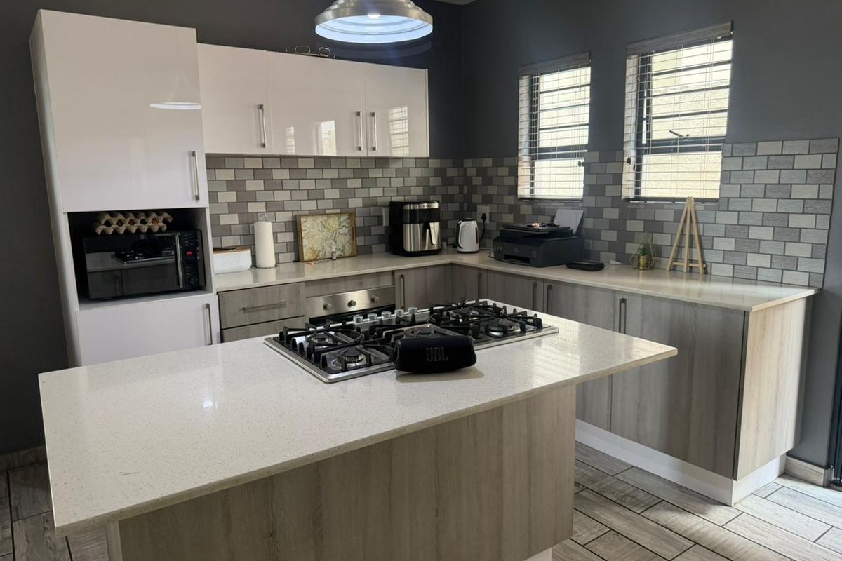 Modern kitchen featuring a central island with a gas hob, quartz countertops, subway tile backsplash, and ample fitted cabinetry.